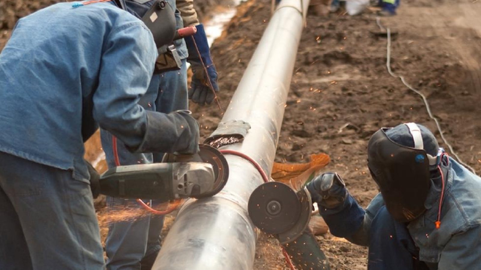 Industrial workers preparing a large pipeline in a construction trench.